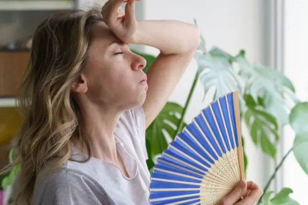 Lady with fan in hand trying to cool off inside